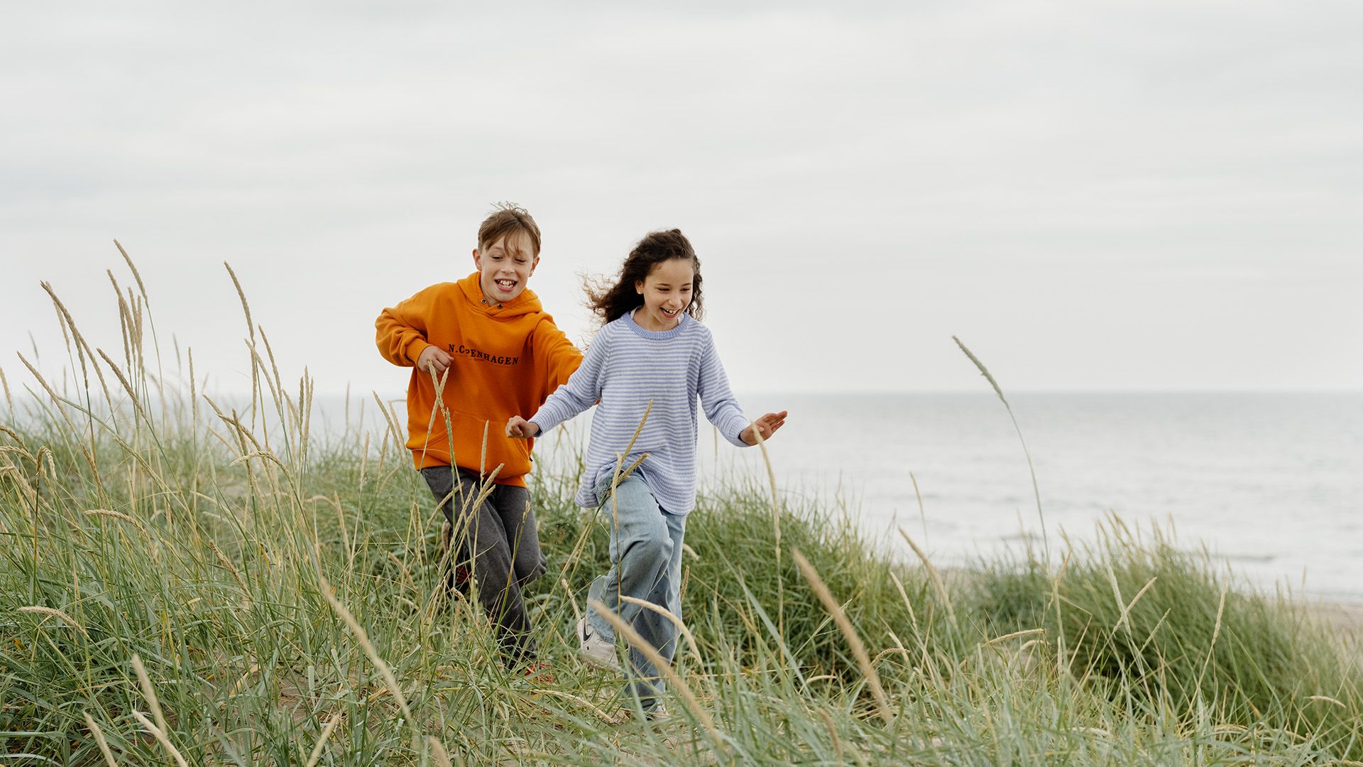 Børn løber og leger på stranden om sommeren, hvor rejseforsikringen også dækker. 
